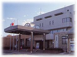 青空の下建つ黒色の玄関庇付き滑川町役場の外観を斜め右のアングルから撮影した写真