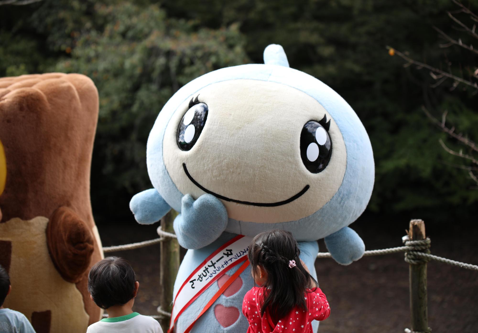 国営武蔵丘陵森林公園内のあざみくぼ沼でおこなわれた沼まつりに遊びに来たターナちゃんが左手で来場者の少女と握手している写真