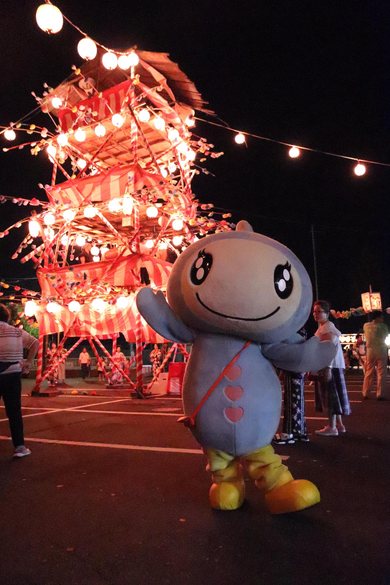 納涼盆踊り大会で提灯の灯りに照らされた大やぐらの前で記念撮影をするターナちゃんの写真