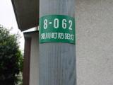 防犯灯に取り付けられた白い字で「8-062滑川町防犯灯」と書かれている緑色の防犯灯プレートの写真